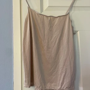 Beiget linne från H&M XS - Säljer ett enkelt och stilrent beiget linne från H&M i storlek XS. Linnet har tunna axelband med rak halsringning. Materialet är mjukt och lätt polyester, perfekt för varma dagar. Passformen är normal.