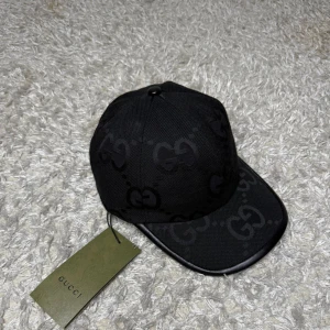 Gucci jumbo keps - Snygg svart keps från Gucci med klassiskt GG-monogram i ton-i-ton över hela kepsen. Kepsen har böjd skärm, justerbar rem baktill och är tillverkad i ett slitstarkt tyg med detaljer i läder. Perfekt accessoar för en trendig streetstyle-look.