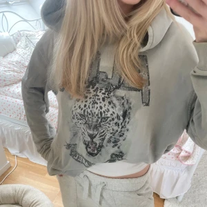 Grå hoodie med leopardtryck från Alix - Säljer en grå hoodie från Alix med stort leopardtryck och texten 'ALIX THE LABEL' framtill. Tröjan har huva, långa ärmar och ribbade muddar. Perfekt för dig som gillar coola djurmotiv och streetstyle. Storlek M plus har lite håll vid armarna men tror dom va så när jag köpte 🌸