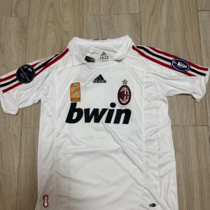 AC Milan Kaka 22 bortatröja Adidas S - AC Milan bortatröja med Kaka 22-tryck, Adidas. Vit med svarta och röda detaljer, klubbmärke och Champions League-patch på ärmen. Broderad Adidas-logga, Bwin sponsortryck och klassisk krage. Tillverkad i polyester, perfekt för fans.