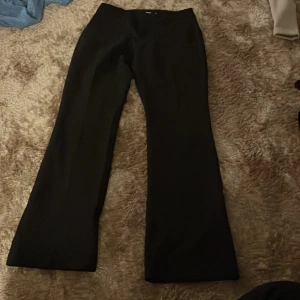 Svarta  kostymbyxor - Svarta kostymbyxor med  lite utsvängt silhuett och låg midja . Byxorna har en klassisk och stilren look, perfekta för dig som gillar en tidlös vibe. Materialet är troligtvis polyester eller bomullsmix, vilket ger en snygg passform och lite stretch.