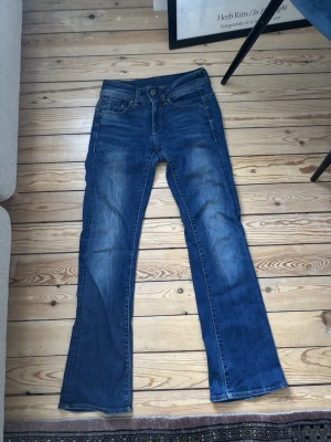 Blå G-star low waist bootcut jeans - Säljer ett par blå bootcut jeans med snygga slitningar och klassisk femficksdesign. Jeansen har normal midja och är tillverkade i denim med lätt stretch för skön passform. Perfekta för dig som gillar en avslappnad men trendig look. Inte helt säker på storlek men troligen 26/30. Säljer då dom är för korta för mig tyvärr💕💕💕