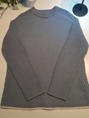 Stickad tröja från Acne Studios - Ljusblå stickad tröja med snygg strukturstickning och ribbade ärmar. Tröjan har rund halsringning och en vit kant längst ner. Perfekt för dig som gillar en stilren och enkel look.