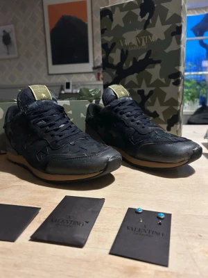 Valentino Garavani camo sneakers - Snygga sneakers från Valentino Garavani i svart och mörkblå färg, riktigt feta för folk som vill sticka ut. Box ingår och lite extra spikar och sånt. Pris kan diskuteras i snabbaffär😇 (tveka inte att höra av dig)