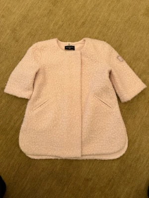 Ljusrosa teddyjacka från Monnalisa - Supersöt ljusrosa teddyjacka från Monnalisa med rund halsringning och trekvartsärmar. Jackan har två snedställda fickor fram och ett litet tygmärke på ärmen. Mjuk, fluffig och perfekt för kyliga dagar.