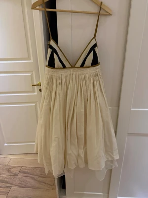 Krämfärgad klänning från by malene Birger - Säljer en luftig klänning med krämfärgad, vippig kjol och triangelformad överdel med svartvita mönster. Klänningen har tunna axelband och markerad midja. Perfekt för dig som gillar en unik och somrig stil. Storlek L men skräddarsydd till en S-M. Färgen åkte igenom tyget under kemtvätt, men syns ej när den är på:)