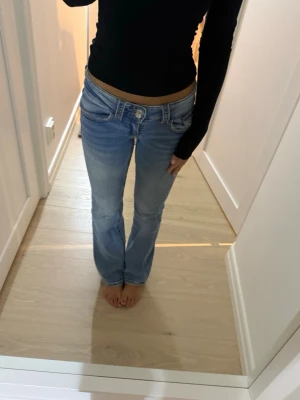 Ljusblå bootcut jeans från Gina 9-14 - Säljer ett par ljusblå bootcut jeans med låg midja och klassiska fem fickor. Jeansen har en snygg tvätt med lätt slitning framtill. Storlek 146-152