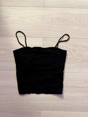Svart croppad linnetopp - En enkel och stilren svart croppad linnetopp från Ginatricot med tunna axelband. Perfekt att matcha med höga jeans eller kjol. Tillverkad i mjuk bomull för en bekväm känsla.