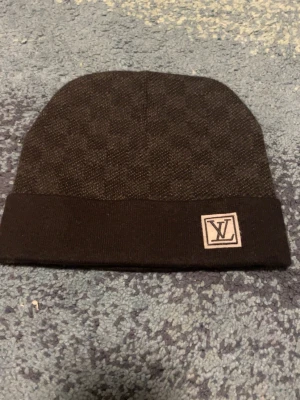 Svart vl  baklänges  - Snygg svart mössa från vl baklänges  med diskret rutmönster och vikt kant. Märkt med vl baklänges -logga framtill. Perfekt accessoar för dig som vill ha en stilren och exklusiv look. Tillverkad i mjukt stickat material som håller dig varm.