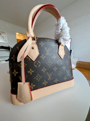 Iouis Vuitton Väska  - Mer än bara en väska , det är en statement-piece. Ta din utstrålning till nästa nivå och låt alla blickar vändas mot dig.