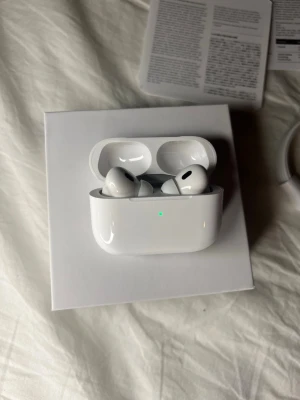 Apple AirPods Pro 2nd Gen vita - Säljer ett par vita Apple AirPods Pro (2nd generation) med laddningsetui. De har en stilren och kompakt design i blank plast och levererar grymt ljud med brusreducering. Perfekta för dig som vill ha trådlösa hörlurar med hög kvalitet och smidig anslutning till Apple-enheter.