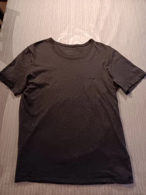Grå t-shirt från BOSS - Säljer en stilren grå t-shirt från BOSS med diskret broderad logga på bröstet. T-shirten har rund halsringning och korta ärmar. Tillverkad i mjuk bomull som känns skön mot huden. Perfekt basplagg till garderoben.