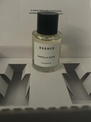ESSNCE Vanilla Sass Eau de Parfum - Parfymflaska från ESSNCE med doften Vanilla Sass. Flaskan är genomskinlig med svart rund kork och vit etikett. Innehåller Eau de Parfum och har en stilren, modern design. Perfekt för dig som gillar söta och mjuka vaniljtoner. Testad en gång