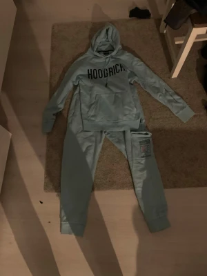 Ljusblå HOODRICH hoodie med matching mjukis byxor  - Snygg ljusblå hoodie från HOODRICH med stor svart logga på bröstet och klassisk känguruficka. Hoodien har huva med dragsko och är tillverkad i mjukt material, perfekt för en avslappnad streetwear-look.Med matching Hoodrich mjukis byxor 