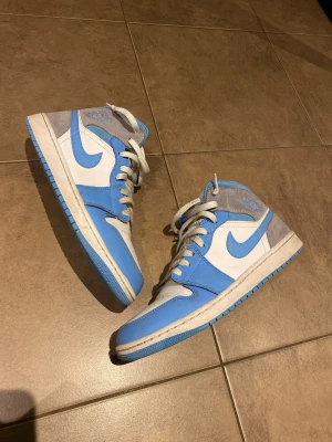 Air Jordan 1 Mid - blå/vita sneakers  - Sjukt snygga Air Jordan 1 Mid sneakers i blå/vit! Mycket bra skick förutom en liten skråma (sista bild) inget som syns elller märks när man har dem på sig, en gnutta smutsiga kanske men inget märkvärdigt . Postar inom 24h📦