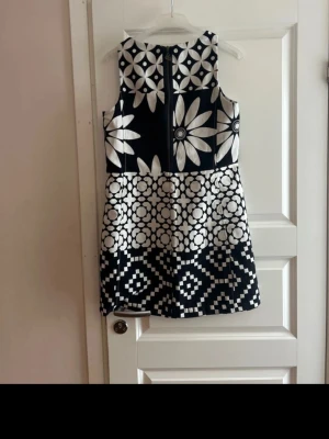 Svartvit mönstrad klänning Desigual - Unik svartvit kortklänning från Desigual med stora blommor och grafiska mönster. Klänningen är ärmlös, har rund hals och dragkedja bak. Materialet känns mjukt och har en lätt glans. Perfekt för dig som gillar statement-plagg och coola prints.. varan har aldrig använts , prislapp finns inte!