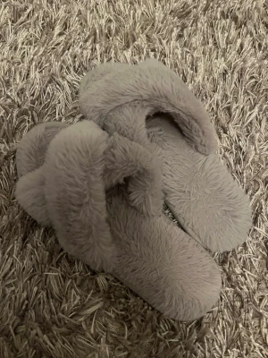Grå fluffiga sandaler strl 35/36 - Supermysiga grå sandaler med fluffig ovandel och mjuk sula. Perfekta att glida runt i hemma för extra komfort. Sulan är i syntetmaterial och ovandelen är täckt av mjuk pälsimitation. Passar dig som gillar cozy vibes. Jag som har på mig dom på bilderna har storlek 37, så de börjar bli lite för små för mig.