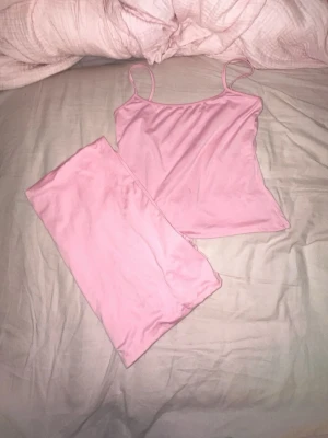 Rosa loungewear set med linne - Säljer ett mjukt och stretchigt rosa loungewear set med ett enkelt linne med smala axelband och matchande lång kjol med låg midja. Perfekt för chill dagar hemma eller mysiga kvällar. Materialet känns lent mot huden och färgen är en söt ljusrosa.