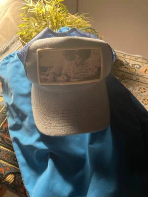 Blå och vit keps med tryck - Snygg keps i blått och vitt från Maggiore med mesh på sidorna och ett unikt svartvitt tryck framtill. Klassisk böjd skärm och justerbar passform. Perfekt för dig som vill sticka ut med en personlig accessoar.