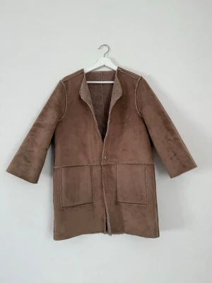 Vändbar jacka H&M – Faux Suede & Faux Fur – XS - Snygg vändbar kappa från H&M i storlek XS. Ena sidan är i mjuk mockaimitation (faux suede) och den andra i varm teddy/fårskinnsimitation (faux fur). Den har tryckknappar och fickor på båda sidor. Två jackor i en, perfekt vårjacka!  Mycket gott skick, inga anmärkningar.