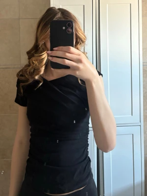 Svart omlottopp med kort ärm - Snygg svart omlottopp med korta ärmar och lätt v-ringad hals. Toppen har en tight passform och är tillverkad i ett stretchigt material som sitter skönt på kroppen. Aldrig använd endast testad❣️