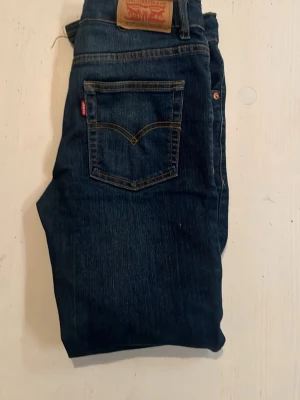 Mörkblå Levi's jeans med klassisk ficka - Säljer ett par mörkblå Levi's jeans med klassisk femficksdesign och den ikoniska röda Levi's-lappen på bakfickan. Jeansen har kontrastsömmar och är tillverkade i slitstark denim. Perfekta för en avslappnad och tidlös stil.