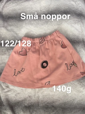 Rosa kjol med hjärtan och text - Söt rosa kjol med svarta broderade hjärtan, ögon och texten 'love' på flera ställen. Kjolen har resår i midjan . Perfekt för dig som gillar gulliga detaljer och en avslappnad stil.🌸 Små noppor. Storlek 122/128