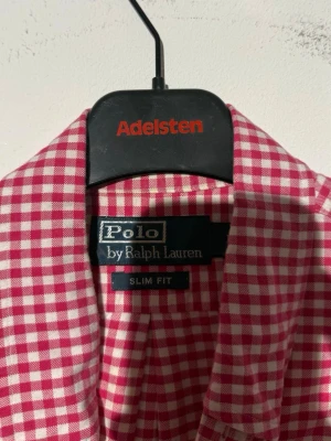 Rutig rosa skjorta från Polo Ralph Lauren - Säljer en slim fit skjorta från Polo Ralph Lauren i rosa och vitt rutigt mönster. Skjortan har klassisk krage, knappar framtill och lång ärm. Tillverkad i mjuk bomull och har den ikoniska broderade loggan på bröstet.