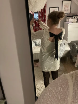 Vit paljettklänning med svart rosett - Jättefin vit paljettklänning med svart rosett i ryggen. Använd 1 gång. Egentligen i storlek M men den passar mig som är XS/S! Priset kan diskuteras🫶🏼 