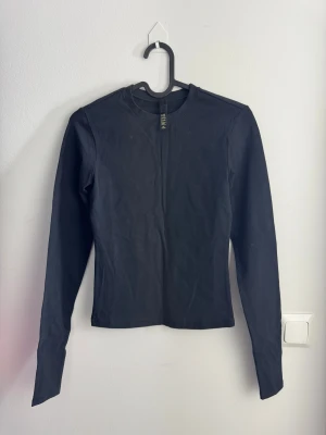 Svart långärmad topp från SKIMS XS - En svart långärmad topp från SKIMS i storlek XS. Modellen är enkel med rund hals och har en slim passform. Materialet är mjuk bomull med lite elastan för extra stretch och komfort. Perfekt att styla med jeans eller kjol för en clean look.