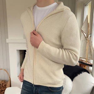 Vit stickad hoodie från Gran Sasso - Säljer en stilren vit stickad hoodie från Gran Sasso. Tröjan har ribbad struktur, dragkedja framtill och huva. Perfekt för dig som gillar en clean och avslappnad look. Tillverkad i mjukt material som känns lyxigt mot huden.