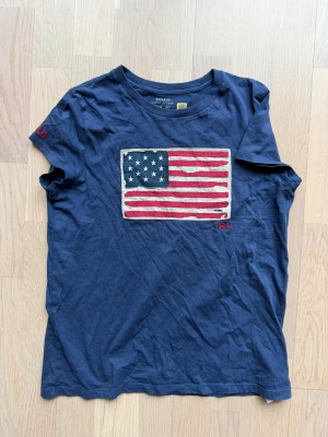 Ralph lauren flag tee size 155/160 - Marinblå T-shirt med flagg motiv från Ralph lauren. Tjejmodell. Passar stl 12-14 år (passar 160-165 cm lång). Eller stl 32-34. 