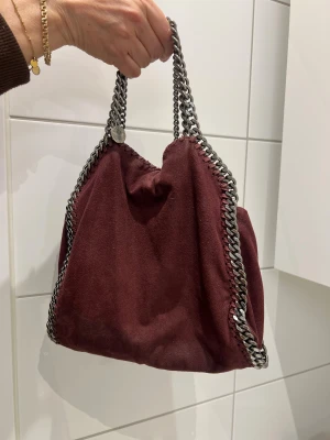 Vinröd axelväska med kedjedetaljer - Super fin väska från Stella McCartney. Vinröd med silver detaljer💞 lite rostig på kedjan och lite missfärgningar här o där men i övrigt bra skick! Inget kvitto eller dustbag men finns på vestiare där noggranna äkthets kontroller genomförs för att garantera äkta vara🫶🏼