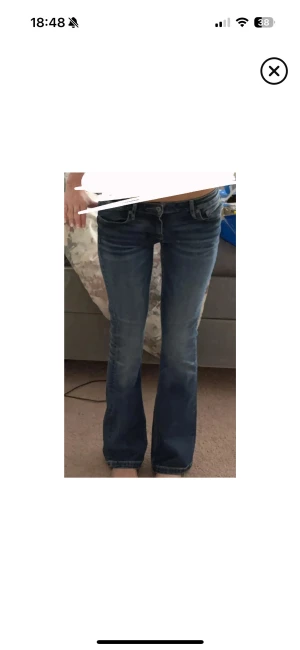 Blå bootcut jeans från Crocker - Snygga blå jeans från Crocker med klassisk bootcut passform och låg midja. Jeansen har slitningar och tvättade detaljer för en cool look, fem fickor och tydliga sömmar. Perfekta för dig som gillar en avslappnad stil med lite edge. Innerbenslängd: 81, midja rakt över: 36cm