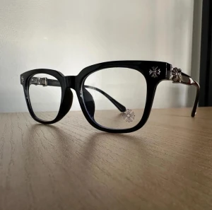 Svarta glasögon med silverdetaljer - Snygga svarta glasögon från Chrome Hearts med rektangulära bågar i plast och coola silverdetaljer på sidorna. Glasen har en diskret blomdekor och bågarna är robusta med en unik design som sticker ut. Helt nytt. fraktar inom 24 timmar. för mer info skriv t mig.