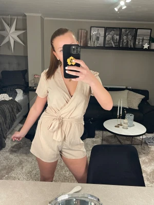 Beige omlottshorts med knytband - Snygga beige shorts med omlottdesign och knytband i midjan. Modellen är högmidjad och har en avslappnad passform. Materialet känns lätt och luftigt, perfekt för varma dagar. Shortsen har en stilren look med korta ben och mjuk struktur.