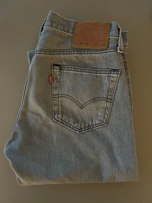 Levi's 501 ljusgrå jeans W30 L32 - Säljer ett par klassiska Levi's 501 jeans i ljusgrå tvätt. Modellen har rak passform, fem fickor och den ikoniska läderpatchen bak i midjan. Jeansen är tillverkade i slitstarkt bomullsdenim och har den röda Levi's-taggen vid bakfickan.