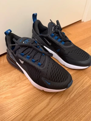 Nike Air Max 270 svart/blå sneakers - Säljer ett par helt oanvända nike 270 i storlek 38,5 i unisex modell. Dessa är endast prövade då jag fick dom i present men inte passade. Funksr perfekt till dig som vill ha en skön fin vardagssko men funkar även till gym och liknande.