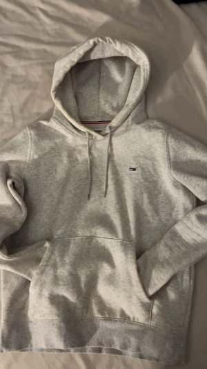 Ljusgrå hoodie Tommy Jeans XS - Säljer en ljusgrå Tommy Hilfiger-hoodie i storlek XS. Den sitter ganska tight om du vanligtvis har S, så perfekt för dig som gillar en mer slimmad passform. Klassisk modell i mjuk bomullsblandning som är riktigt skön att ha på sig. Hoodien är använd men fortfarande bekväm och fin i formen. Det finns några mindre fläckar vid huvan, halsen, ena ärmen och fickorna. Inget som syns direkt man märker det mest om man kommer riktigt nära eller fotar med blixt, vilket är vanligt med ljusgrått tyg.