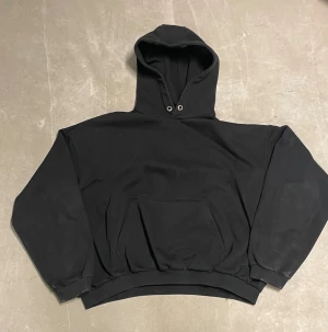 Svart oversized hoodie med huva - Svart hoodie i oversized modell med stor huva och klassisk magficka. Tröjan har ribbade muddar vid ärmslut och nederkant, samt metallöljetter vid snörningshålen. Perfekt för chill dagar och enkel att matcha med allt.