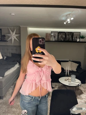 Rosa volangig blus med knyt - Supersöt rosa blus med volanger och knyt framtill. Plisserad och luftig modell med v-ringning och ärmlös design. Perfekt för dig som gillar romantisk och feminin stil.