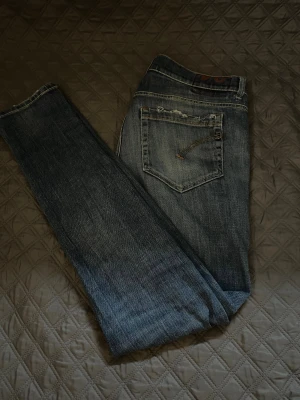 Blå jeansbyxor från Dondup med raka ben - Säljer ett par klassiska blå jeans från Dondup i modellen GEORGE, med raka ben och snygga slitningar på bakfickorna. Priset är inte spikat, Jeansen har fem fickor, mörk tvätt som ger en cool vintagekänsla. Perfekta för dig som gillar en tidlös och avslappnad stil.