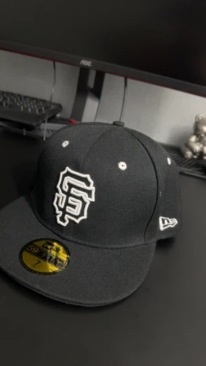Svart San Francisco Giants keps New Era - Snygg svart 59FIFTY keps från New Era med San Francisco Giants logga broderad i vitt framtill och 'SAN FRANCISCO' tryckt under skärmen. Klassisk form med platt skärm och broderade ventilationshål. Perfekt för dig som gillar streetwear och sport. Kontakta gärna för  funderingar🤩