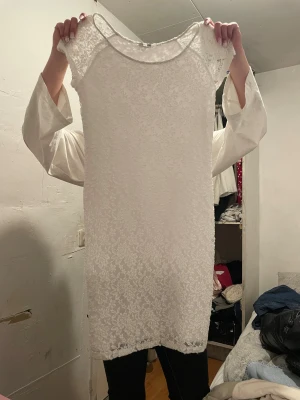 Vit spetsklänning från KappAhl - Supersöt vit kortklänning från KappAhl i storlek M. Klänningen har ett blommigt spetsmönster och är ärmlös med rundad hals. Perfekt för dig som gillar romantisk stil och vill ha något ljust och fräscht i garderoben.