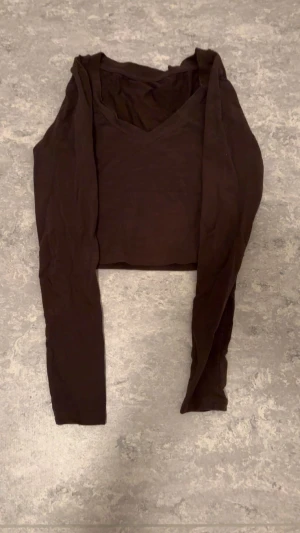 Brun croppad långärmad topp - Säljer en brun croppad topp med lång ärm och v-ringad hals. Enkel och stilren design som passar perfekt till jeans eller kjol. Tunn och mjuk i materialet för en bekväm känsla.
