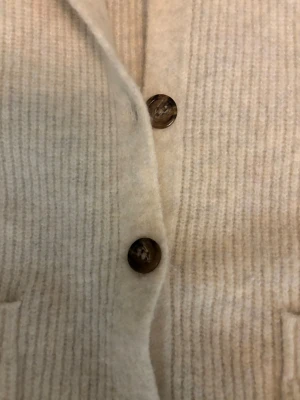 Beige ribbad kofta från Uniqlo XS - Supermysig beige kofta från Uniqlo i storlek XS. Koftan är ribbstickad med stora bruna knappar och har två praktiska fickor framtill. Den har en loose passform och är tillverkad i mjuk ullblandning, perfekt för lager-på-lager under höst och vinter. Köpte den för 500kr