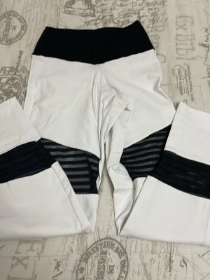 Vita och svarta leggings från Bia Brazil - Snygga vita leggings från Bia Brazil med bred svart midja och coola svarta mesh-detaljer på benen. Perfekta för träning eller chill dagar. Stretchigt material som sitter skönt och formar sig efter kroppen.