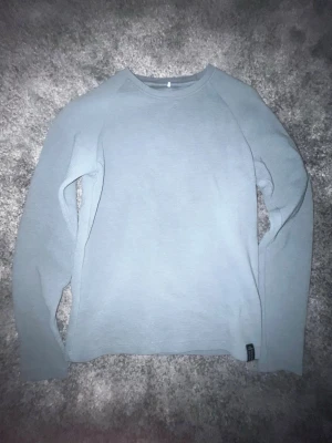 Grå långärmad tröja från Name It - En enkel och stilren grå långärmad tröja från Name It. Tillverkad i mjuk bomull, perfekt för lager på lager under höst och vinter. Tröjan har rund halsringning och en diskret liten etikett nertill.