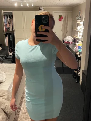 Ljusblå ribbad kortklänning - Snygg ljusblå kortklänning med ribbad struktur och rund hals. Klänningen har korta ärmar och en tight passform som framhäver figuren. Perfekt för dig som gillar enkel och stilren design. Materialet känns mjukt och stretchigt mot kroppen.