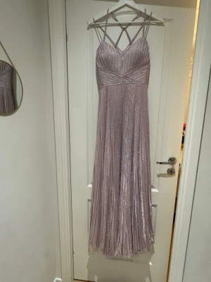 Ljusrosa glittrig långklänning - Supersnygg ljusrosa långklänning med tunna axelband i korsad design och glittrigt tyg. Klänningen har plisserad kjol och v-ringad urringning, perfekt för bal eller fest. Materialet känns mjukt och skimrande, och den har en elegant siluett som verkligen sticker ut.